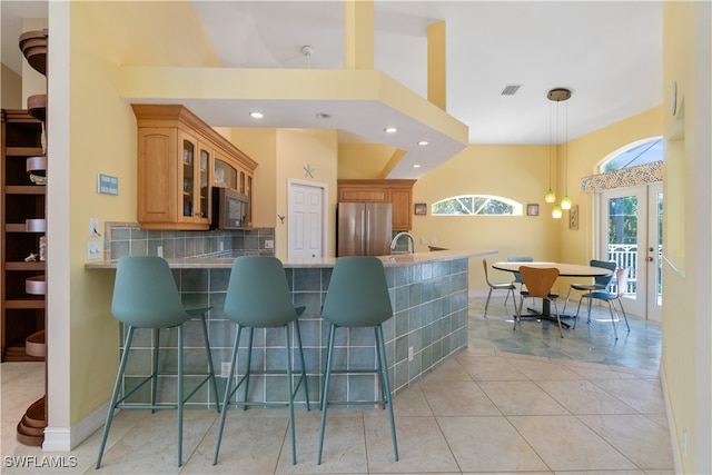 kitchen featuring a kitchen breakfast bar, backsplash, kitchen peninsula, pendant lighting, and appliances with stainless steel finishes