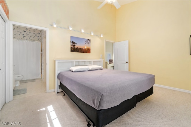 bedroom featuring a high ceiling, light colored carpet, ensuite bath, and ceiling fan