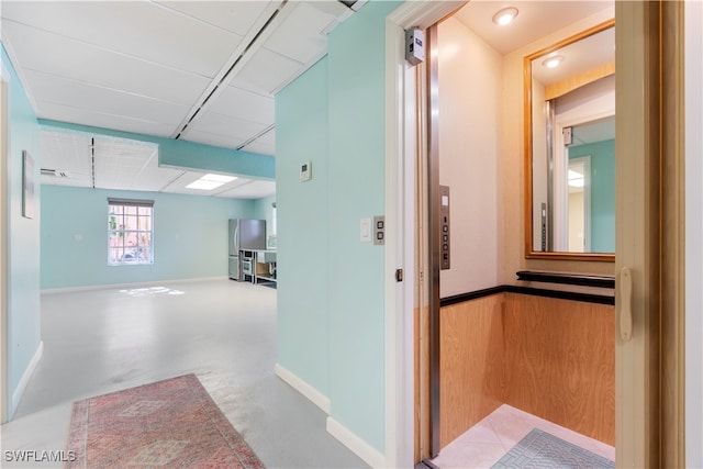 corridor with elevator, wooden walls, and concrete floors