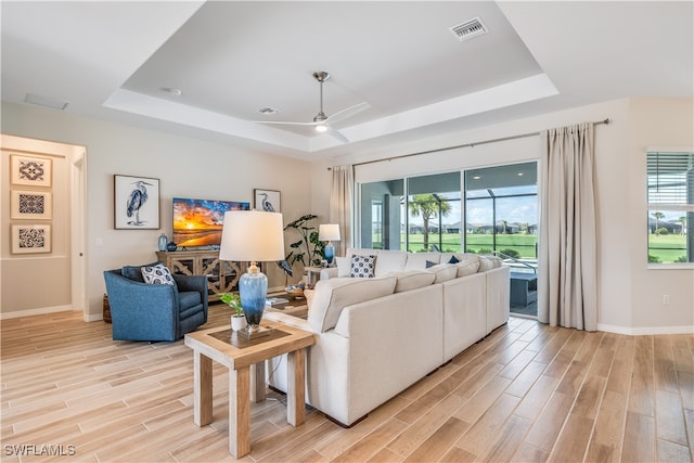 living room with a tray ceiling, ceiling fan, and light hardwood / wood-style flooring