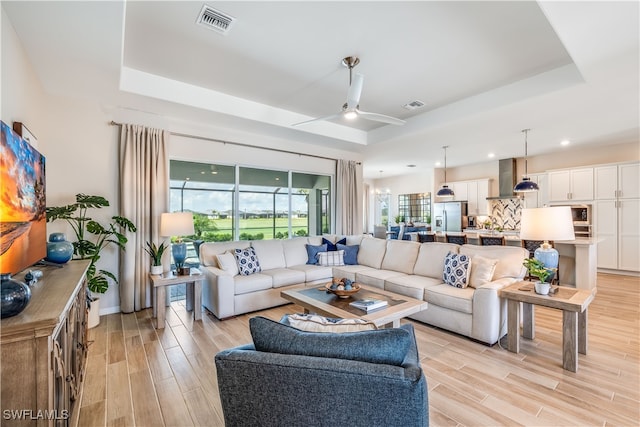 living room with ceiling fan, a tray ceiling, and light hardwood / wood-style floors