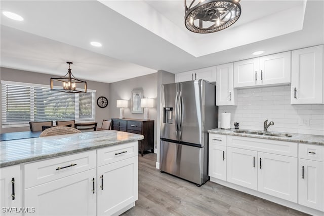 kitchen featuring white cabinetry, sink, decorative light fixtures, light hardwood / wood-style flooring, and stainless steel fridge