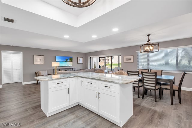 kitchen featuring light wood-type flooring, white cabinetry, decorative light fixtures, and light stone counters