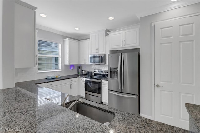 kitchen with appliances with stainless steel finishes, white cabinetry, dark stone counters, and sink