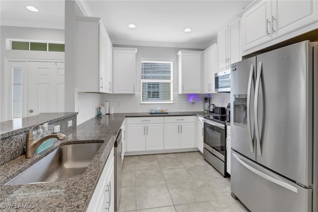 kitchen featuring appliances with stainless steel finishes, sink, dark stone countertops, white cabinetry, and light tile patterned flooring