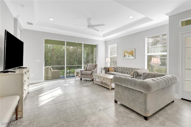 tiled living room with a raised ceiling, ceiling fan, and plenty of natural light