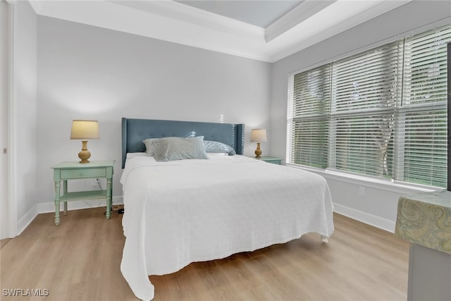 bedroom featuring light wood-type flooring, ornamental molding, a tray ceiling, and multiple windows