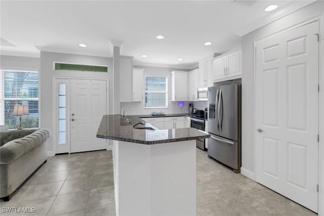 kitchen with white cabinetry, kitchen peninsula, dark stone countertops, crown molding, and appliances with stainless steel finishes