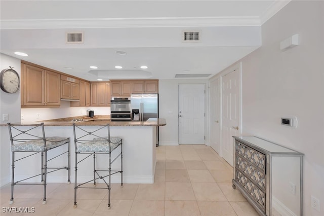 kitchen with light tile patterned flooring, crown molding, appliances with stainless steel finishes, a breakfast bar area, and kitchen peninsula