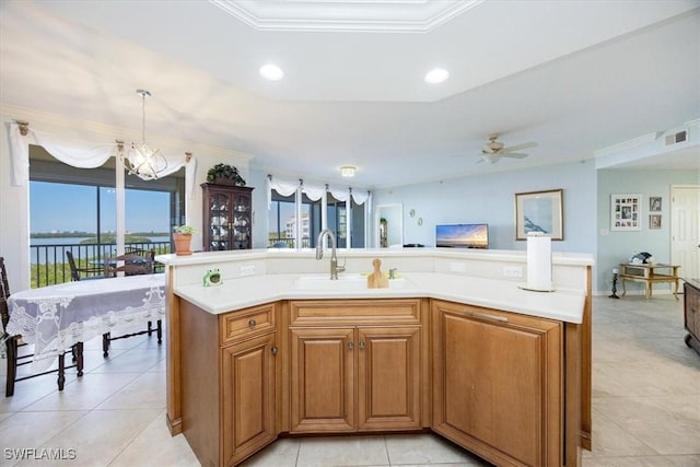 kitchen with sink, hanging light fixtures, a center island with sink, ceiling fan with notable chandelier, and ornamental molding