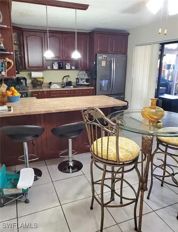 kitchen with sink, a breakfast bar, light tile patterned floors, stainless steel fridge with ice dispenser, and pendant lighting