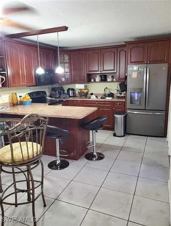 kitchen with black appliances, kitchen peninsula, a breakfast bar area, light tile patterned floors, and hanging light fixtures