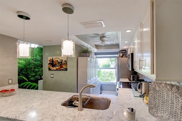 kitchen featuring sink, light stone counters, ceiling fan, decorative light fixtures, and a raised ceiling