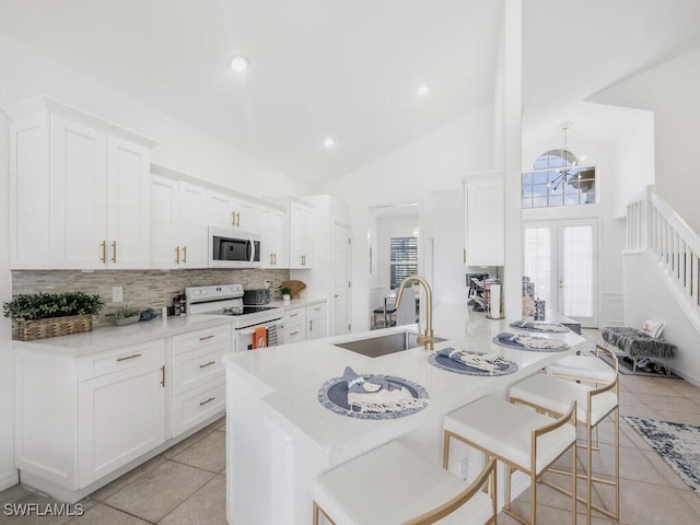 kitchen with a breakfast bar, white appliances, white cabinets, sink, and light tile patterned floors