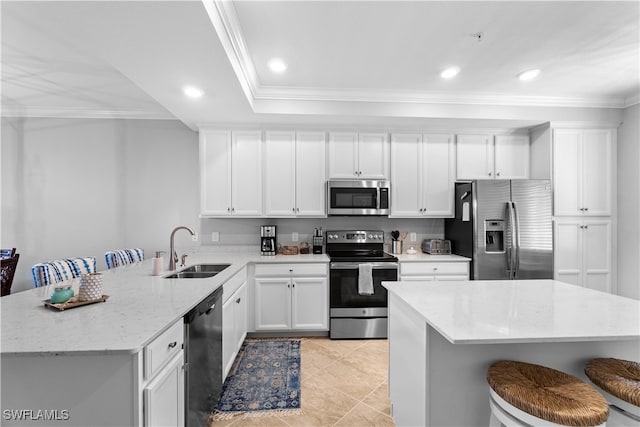 kitchen with light stone counters, stainless steel appliances, white cabinetry, sink, and a kitchen breakfast bar