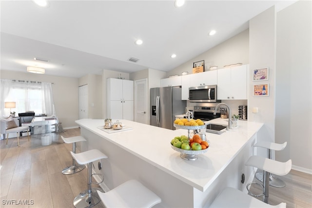 kitchen with lofted ceiling, white cabinets, light hardwood / wood-style flooring, appliances with stainless steel finishes, and a breakfast bar area