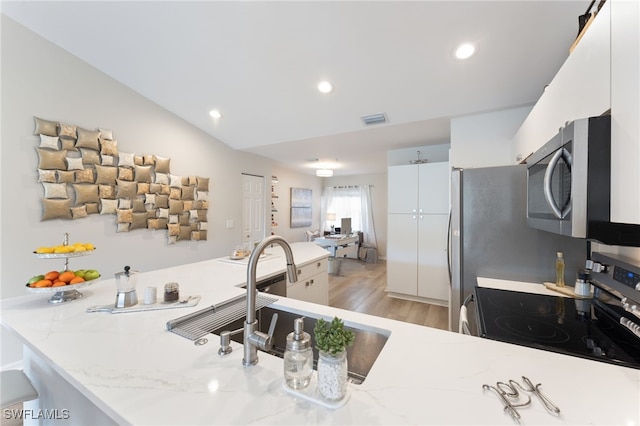 kitchen with white cabinetry, stainless steel appliances, light stone counters, vaulted ceiling, and light wood-type flooring