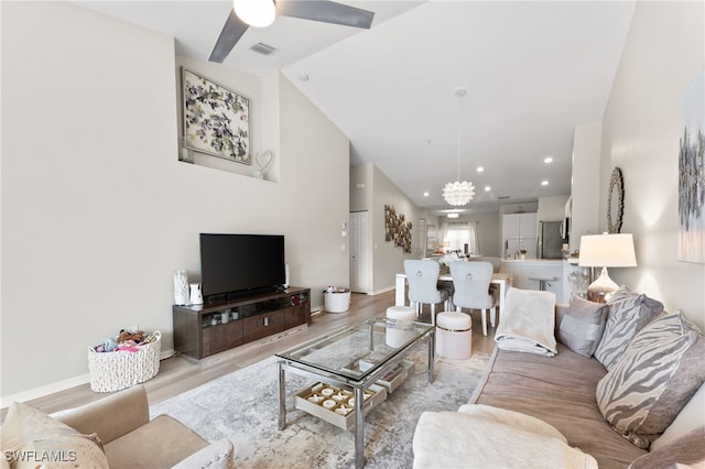 living room with ceiling fan with notable chandelier, vaulted ceiling, and light hardwood / wood-style flooring