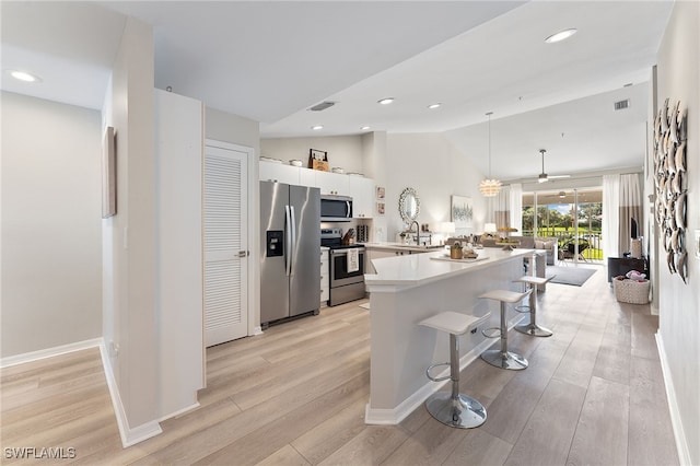 kitchen featuring white cabinets, a kitchen breakfast bar, hanging light fixtures, appliances with stainless steel finishes, and light hardwood / wood-style floors