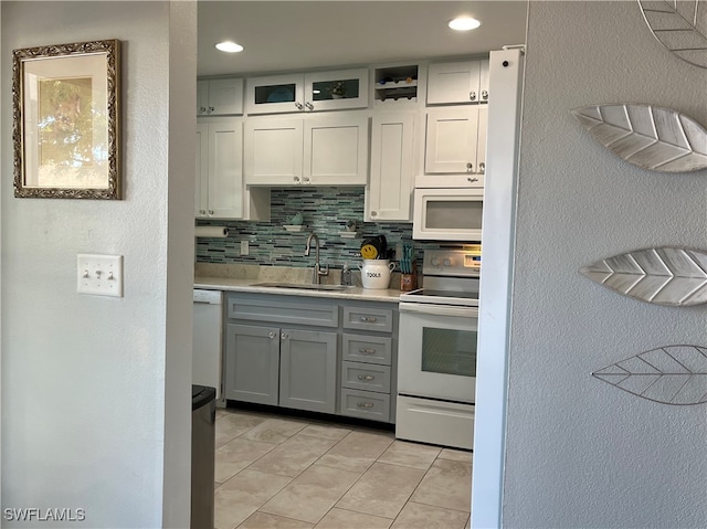 kitchen with light countertops, backsplash, glass insert cabinets, a sink, and white appliances