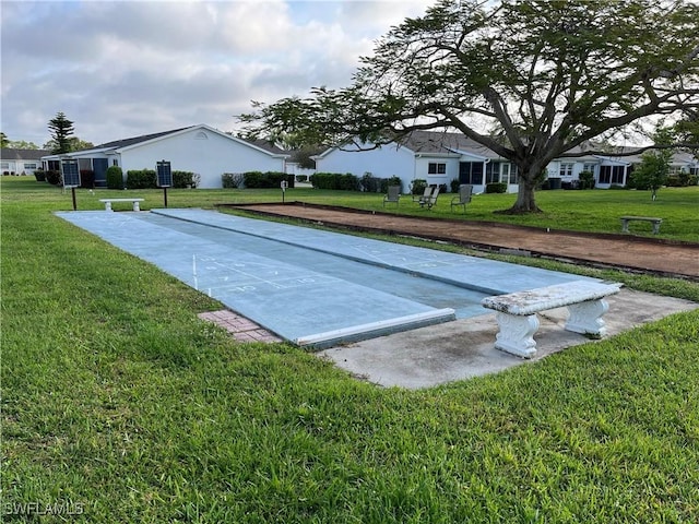 view of community with driveway, shuffleboard, and a yard