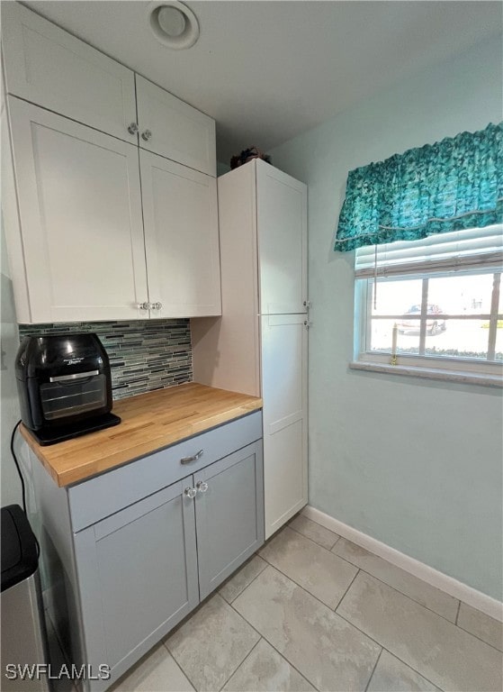 kitchen featuring baseboards, wood counters, white cabinetry, backsplash, and light tile patterned flooring