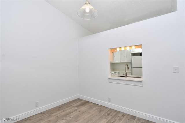 unfurnished room featuring vaulted ceiling, light hardwood / wood-style flooring, a textured ceiling, and sink