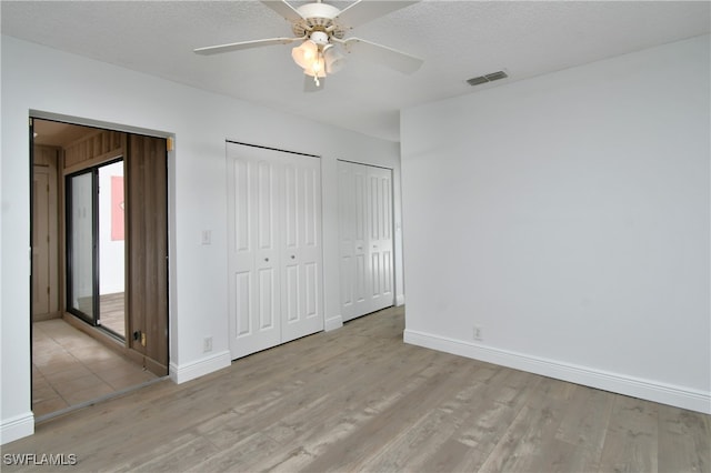 unfurnished bedroom with two closets, ceiling fan, light hardwood / wood-style floors, and a textured ceiling