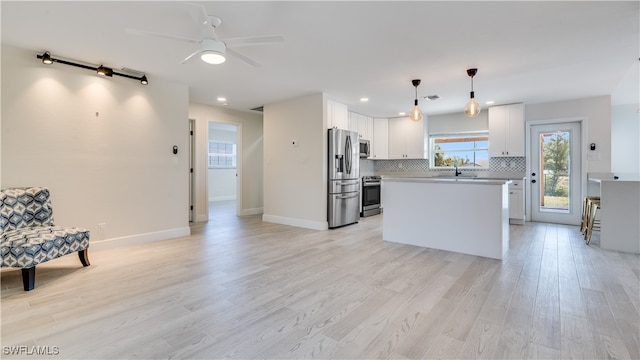 kitchen featuring stainless steel appliances, pendant lighting, a kitchen island, white cabinetry, and light hardwood / wood-style flooring