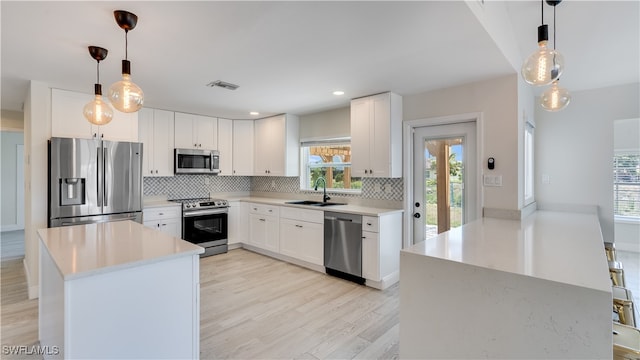 kitchen featuring appliances with stainless steel finishes, pendant lighting, sink, white cabinets, and light hardwood / wood-style flooring