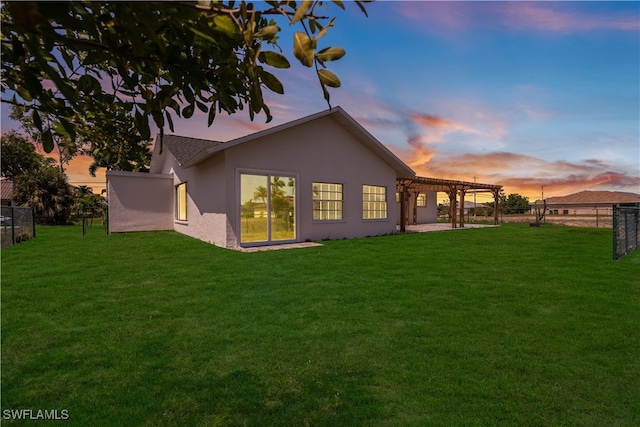 back house at dusk with a pergola and a lawn