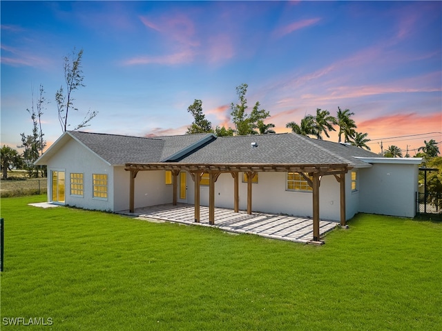 back house at dusk featuring a patio, a pergola, and a lawn