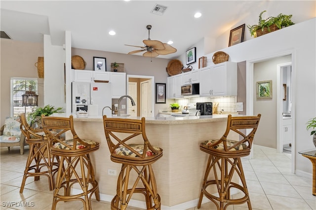 kitchen featuring a kitchen breakfast bar, white cabinetry, white fridge with ice dispenser, and light tile patterned floors