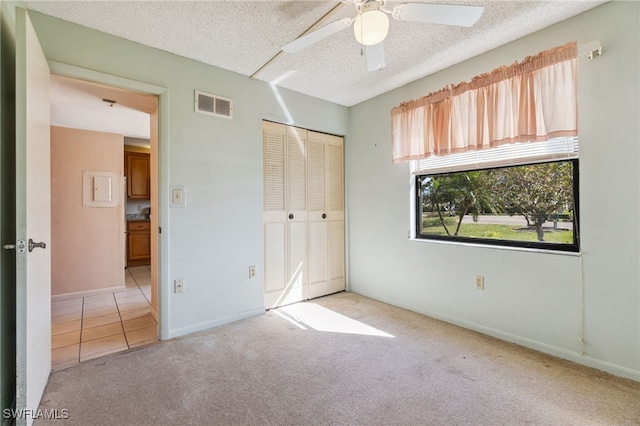 unfurnished bedroom with a textured ceiling, light colored carpet, a closet, and ceiling fan