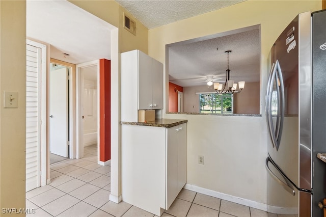 kitchen with light tile patterned floors, a textured ceiling, decorative light fixtures, white cabinetry, and stainless steel refrigerator