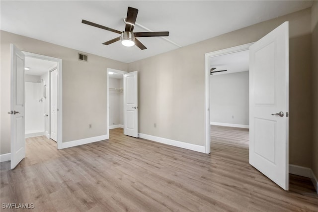 unfurnished bedroom featuring ceiling fan, light hardwood / wood-style floors, a walk in closet, and a closet