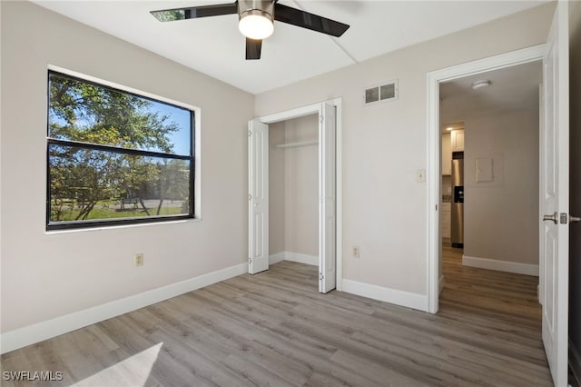 unfurnished bedroom with ceiling fan, a closet, stainless steel refrigerator with ice dispenser, and light hardwood / wood-style flooring