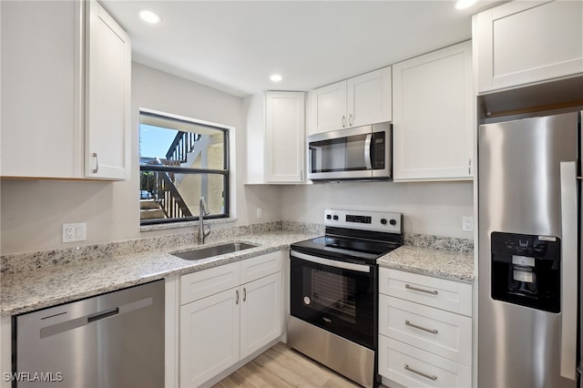 kitchen with white cabinetry, sink, light stone countertops, light hardwood / wood-style flooring, and appliances with stainless steel finishes