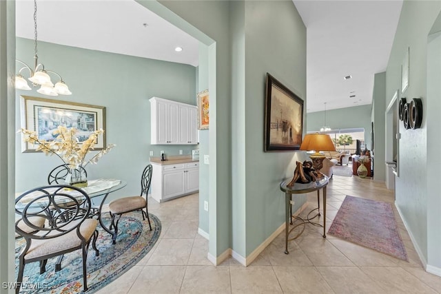 corridor featuring light tile patterned flooring, high vaulted ceiling, baseboards, and a chandelier