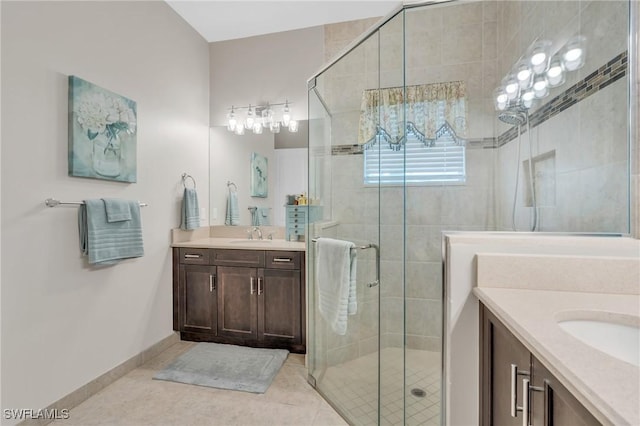 full bathroom with a stall shower, baseboards, two vanities, tile patterned floors, and a sink