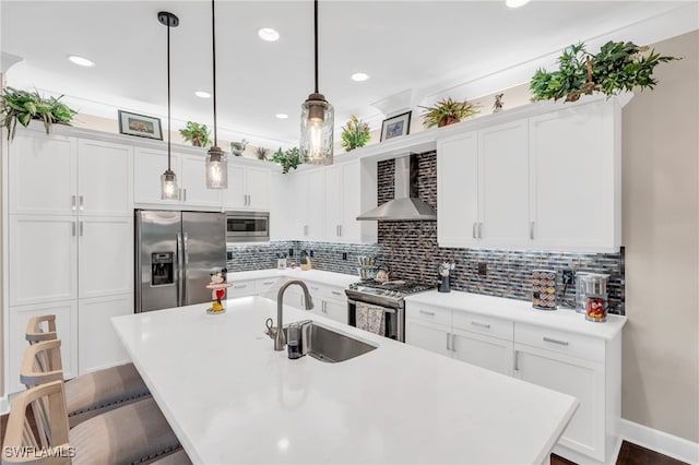 kitchen with sink, wall chimney exhaust hood, an island with sink, pendant lighting, and appliances with stainless steel finishes