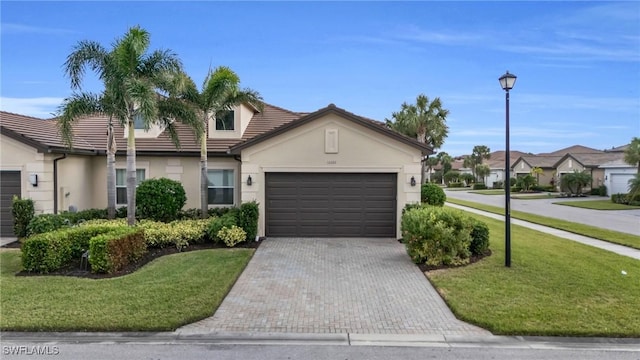 view of front of property featuring decorative driveway, a tile roof, stucco siding, a front yard, and a garage