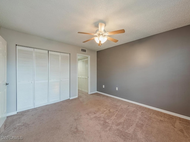 unfurnished bedroom with ceiling fan, a closet, light carpet, and a textured ceiling