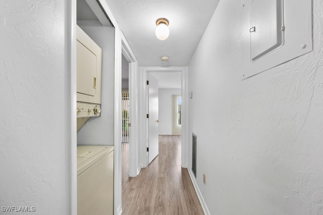 corridor featuring electric panel, stacked washer and dryer, and light hardwood / wood-style flooring