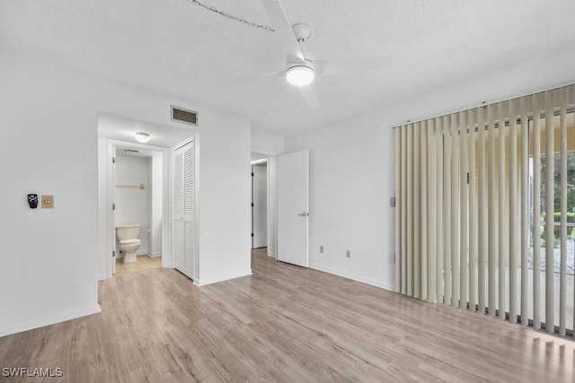 unfurnished bedroom featuring a textured ceiling, light wood-type flooring, ensuite bathroom, and ceiling fan