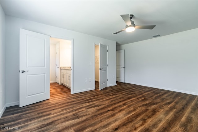 unfurnished bedroom with a closet, a spacious closet, connected bathroom, dark hardwood / wood-style floors, and ceiling fan