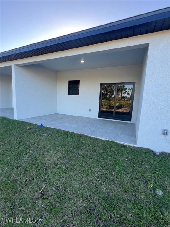 view of exterior entry featuring a lawn and a patio