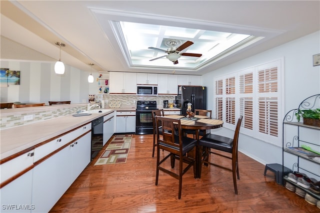 kitchen featuring tasteful backsplash, pendant lighting, white cabinets, black appliances, and hardwood / wood-style flooring