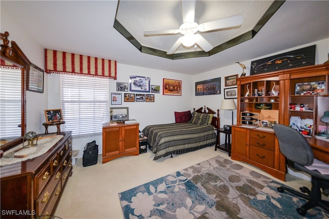 carpeted bedroom with a raised ceiling and ceiling fan