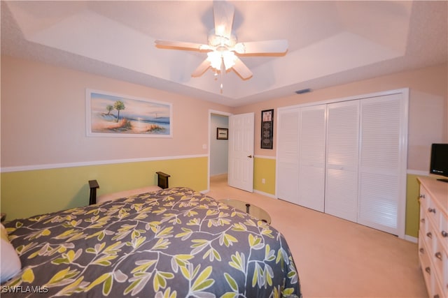 carpeted bedroom with ceiling fan, a raised ceiling, and a closet